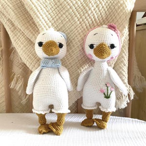 Charming close-up of both amigurumi crochet goose dolls, side-by-side, capturing their adorable facial expressions and handcrafted details. A delightful pair for any child's collection.