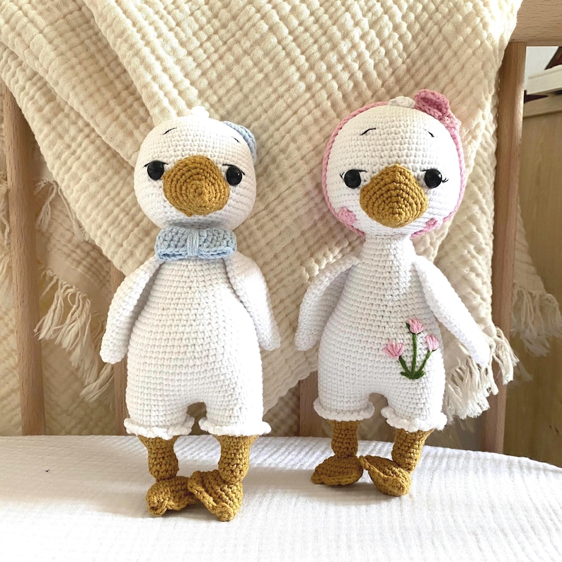 Charming close-up of both amigurumi crochet goose dolls, side-by-side, capturing their adorable facial expressions and handcrafted details. A delightful pair for any child's collection.
