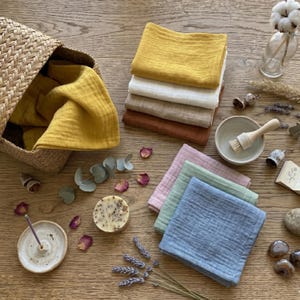 Flat lay of colorful soft muslin face towels with botanical spa accessories, incense and soap. Handmade organic cotton washcloths, reusable makeup remover pads, eco-friendly beauty essentials, rustic bathroom decor handkerchiefs.