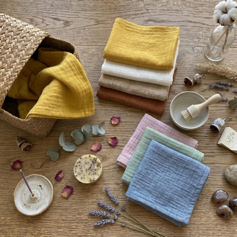 Flat lay of colorful soft muslin face towels with botanical spa accessories, incense and soap. Handmade organic cotton washcloths, reusable makeup remover pads, eco-friendly beauty essentials, rustic bathroom decor handkerchiefs.