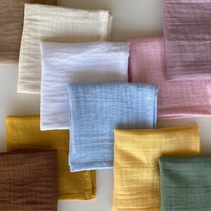 Scattered flat lay of washable organic cotton pocket squares. Detail shot highlighting the crinkle texture and hemmed edges of eco-friendly unpaper tissues in various solid colors.