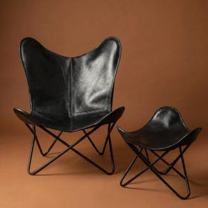 Könnte beinhalten: Ein schwarzer Leder-Schmetterlingsstuhl und ein passender Hocker. Der Stuhl hat eine markante geschwungene Rückenlehne und Sitzfläche, getragen von einem schwarzen Metallrahmen. Der Hocker spiegelt das Design des Stuhls wider.