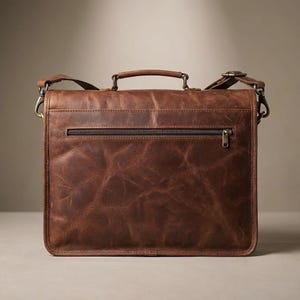 May include: A brown leather briefcase with a top handle, shoulder strap, and a front zipper pocket. The bag has a distressed finish, giving it a vintage look. The hardware is a brass color.