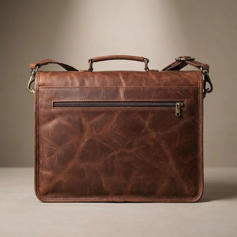 May include: A brown leather briefcase with a top handle, shoulder strap, and a front zipper pocket. The bag has a distressed finish, giving it a vintage look. The hardware is a brass color.