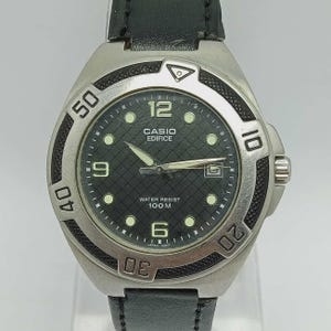 May include: A silver Casio Edifice watch with a black dial and a black leather band. The watch face features white numerals, luminous markers, and the text "WATER RESIST 100 M". The bezel has numbers from 10 to 50.