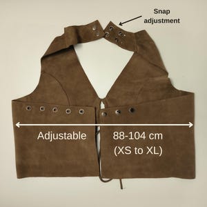 Może przedstawiać: Brązowa zamszowa kamizelka z regulacją na zatrzaski i oczkami. Kamizelka jest regulowana i mierzy 88-104 cm (XS do XL). Kamizelka ma dekolt w kształcie litery V i jest odpowiednia dla r&oacute;żnych typ&oacute;w sylwetki.