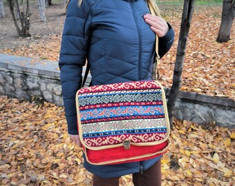 Könnte beinhalten: Eine rote und gemusterte Messenger-Tasche mit Klappenverschluss. Die Tasche hat ein farbenfrohes geometrisches Design in Blau, Rot und Creme. Die Tasche wird über der Schulter mit einem beigefarbenen Riemen getragen.