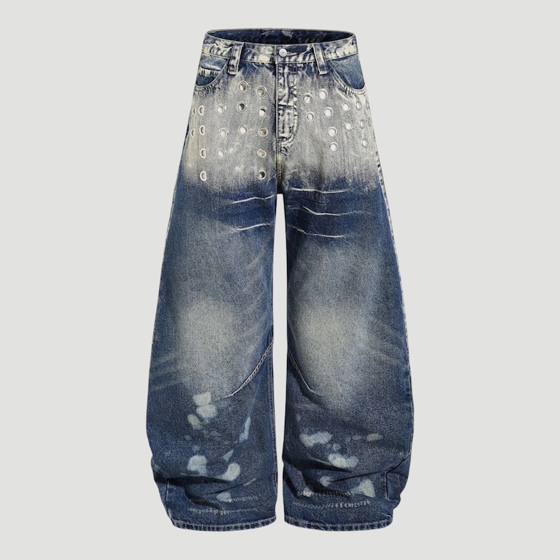 May include: Blue denim jeans with a wide leg design. The jeans feature a faded wash with distressed details, including circular cutouts near the waist and white paint splatters. The jeans have a classic five-pocket design.