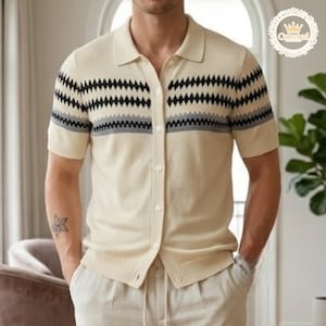 May include: Cream-colored short-sleeve polo shirt with a geometric pattern in black and gray. The shirt has a button-down front and a collared neckline. The shirt is paired with light-colored pants.