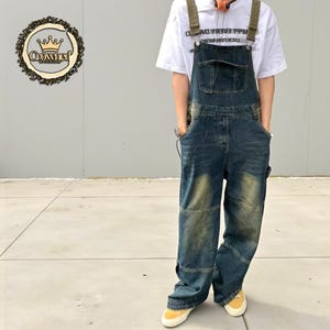 May include: Blue denim overalls with a faded wash and multiple pockets. The overalls have adjustable straps and are worn with a white t-shirt and yellow sneakers. The overalls are a relaxed fit.