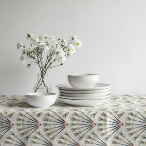 May include: A stack of white ceramic plates and bowls are arranged on a patterned tablecloth. A clear glass vase holds white flowers. The table setting is simple and elegant, perfect for a dining room.