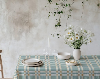 Könnte beinhalten: Ein Esstisch mit einer blau-beige karierten Tischdecke. Der Tisch ist mit weißen Tellern, einer Schüssel und einer Vase mit weißen Blumen gedeckt. Eine brennende Kerze und Gläser sind ebenfalls vorhanden.