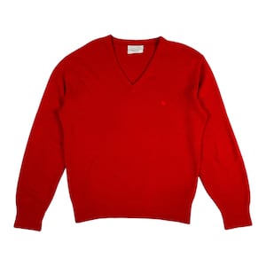 Può includere: Un maglione rosso brillante con scollo a V e maniche lunghe. Un piccolo logo è visibile sul petto. L'etichetta all'interno del colletto è visibile. Il maglione è realizzato in un materiale morbido.