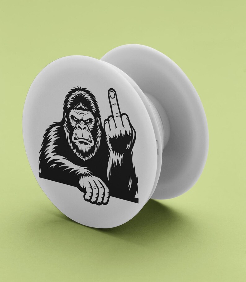 May include: White pop-up phone grip featuring a black and white illustration of a gorilla giving the middle finger. The gorilla is depicted with a stern expression and detailed fur. The grip is round with a collapsible design.