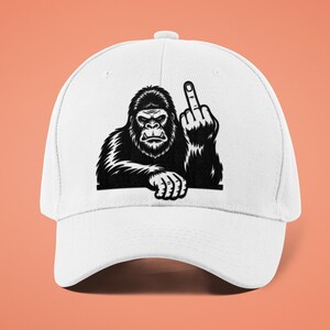 May include: White baseball cap featuring a black and white illustration of a gorilla giving the middle finger. The gorilla is depicted with detailed fur and a stern expression. The cap has a curved brim and a button on top.