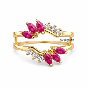 May include: A gold ring guard featuring two curved bands connected at the sides. The design includes marquise-cut vibrant pink stones and round brilliant-cut clear stones arranged in a symmetrical pattern. The text Kweengems is visible on the band.