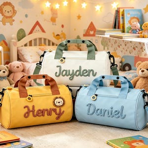 May include: Three personalised duffel bags in a child's room. The bags are yellow, white, and blue, each with a name embroidered on the front. The yellow bag has a lion patch. Each bag has a top handle and a shoulder strap.