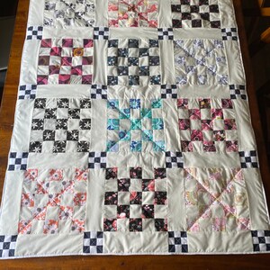 May include: A white quilt with a checkerboard pattern border. The quilt is made up of 12 smaller squares, each with a different floral pattern. The quilt is perfect for adding a touch of elegance to any room.