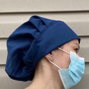 May include: A dark blue scrub cap with a gathered top. The cap is worn by a person wearing a light blue face mask.