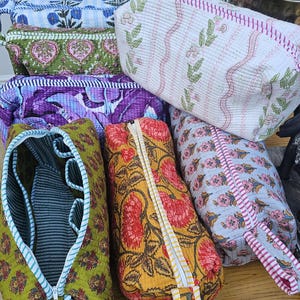 May include: A collection of six rectangular quilted fabric pouches featuring various floral and botanical block-print patterns in colours including white, green, purple, yellow, and light blue, each with a zippered closure and a fabric pull tab.