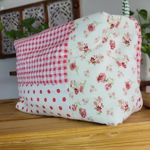 May include: A patchwork fabric storage bag with a red and white gingham pattern, red polka dots, and a floral print. The bag is sitting on a wooden surface.