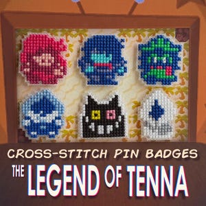 May include: A framed display of six cross-stitch pin badges. The badges depict pixelated characters in red, blue, green, black, and white. Text at the bottom reads "CROSS-STITCH PIN BADGES" and "THE LEGEND OF TENNA".