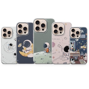 May include: Five phone cases with astronaut-themed designs. Each case features a different illustration of an astronaut on the moon or in space, with various color schemes including blue, green, and pink. The cases are designed to fit a smartphone.