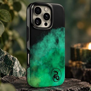Op de afbeelding: Een zwarte smartphonehoes met een levendig groen rookeffectpatroon dat van donker aan de bovenkant overgaat in een lichtere tint aan de onderkant. Een klein, rond zwart icoon met een opgerolde slang is rechtsonder op de hoes gedrukt.