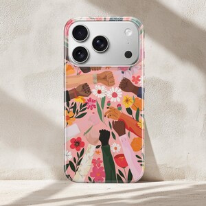 Puede incluir: Una funda para smartphone con fondo rosa y un patr&oacute;n de pu&ntilde;os levantados en varios tonos de piel, intercalados con flores coloridas y hojas verdes. El dise&ntilde;o incluye m&uacute;ltiples brazos y manos que se extienden hacia arriba entre elementos florales.