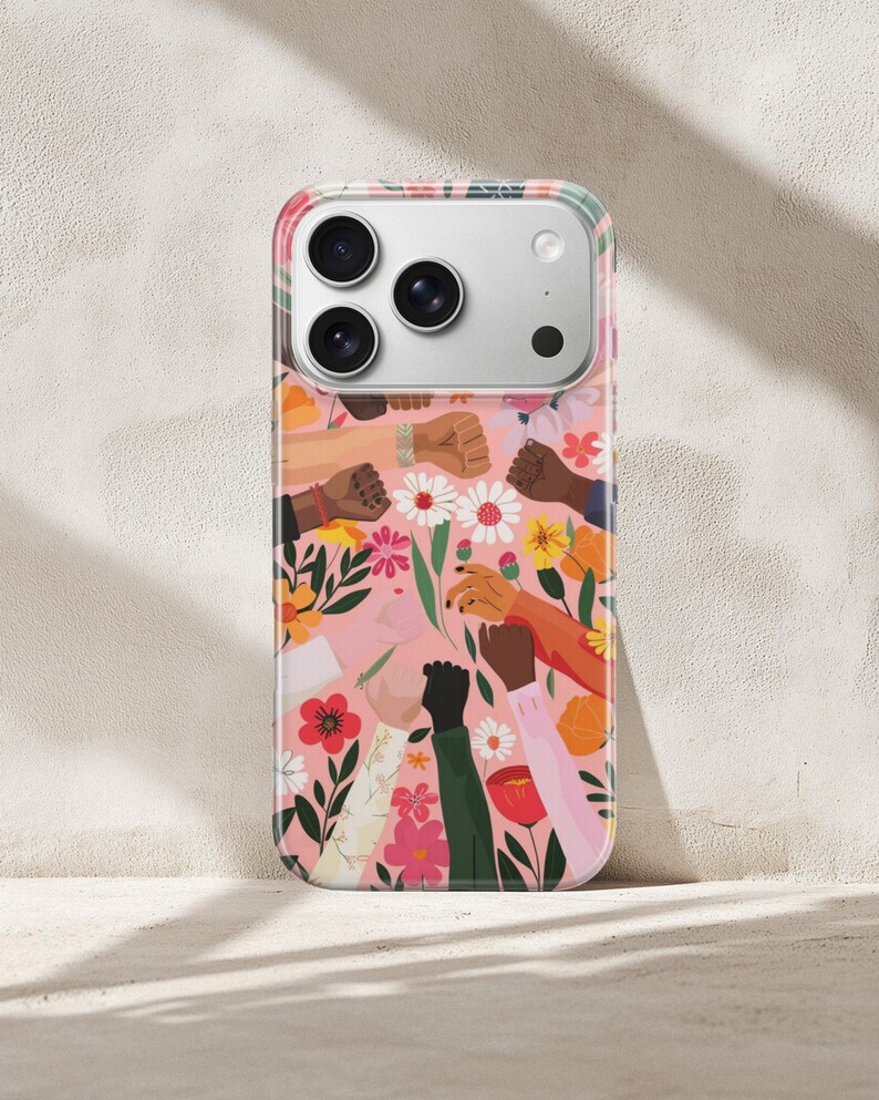 Puede incluir: Una funda para smartphone con fondo rosa y un patr&oacute;n de pu&ntilde;os levantados en varios tonos de piel, intercalados con flores coloridas y hojas verdes. El dise&ntilde;o incluye m&uacute;ltiples brazos y manos que se extienden hacia arriba entre elementos florales.