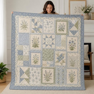 May include: A rectangular quilt featuring a patchwork design with various floral prints, gingham patterns, and geometric blocks in shades of blue, sage green, and cream. The quilt is bordered by a blue floral fabric and has visible stitching.