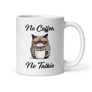 Peut inclure: Une tasse à café en céramique blanche avec un dessin animé de chat grognon tenant une tasse de café. Le texte sur la tasse est "No Coffee, No Talkie".