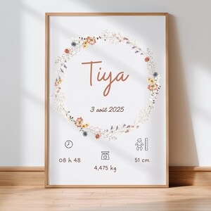 Puede incluir: Un cuadro enmarcado con el nombre "Tiya" en letra cursiva, rodeado por una corona floral. La impresión incluye la fecha "3 août 2025", la hora, el peso de 4,475 kg y una altura de 51 cm. El marco es de color marrón claro.