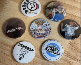 Könnte beinhalten: Eine Sammlung von sieben runden Ansteckbuttons mit verschiedenen Hunde-Grafikdesigns. Die Buttons zeigen Illustrationen und Texte, darunter Bark-182, Stick Bones, Boxer Car Chaser, Green Stray, Pawamor Sit Down, Dogscendents und Aquapups.