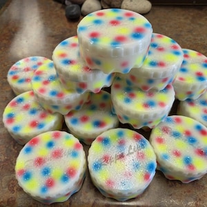May include: A stack of round, white plastic herb grinders featuring a colorful pattern of red, blue, and yellow dots. Each grinder has a textured, scalloped edge and the text "Zippa Life" is embossed on the top surface of several units.