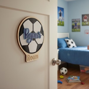 May include: A wooden sign in the shape of a football, with the name "Ryan's" in blue script, and the word "Room" below. The sign is fixed to a white door. The football design has black and white pentagons.