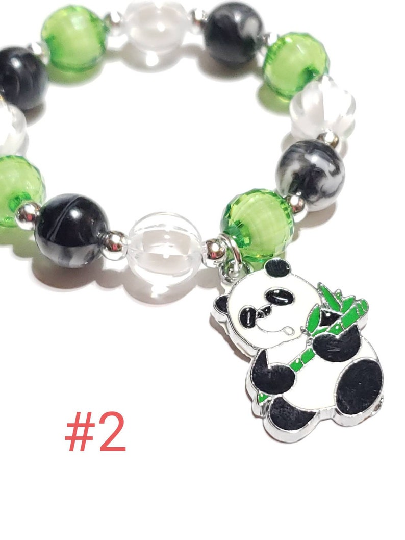 May include: A green, black, and white beaded bracelet with a panda bear charm holding a piece of bamboo. The charm is silver with black and white enamel. The bracelet has a clear bead and the text #2.