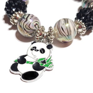 May include: A silver charm bracelet with black and white swirl beads, black crystal beads, and a panda bear charm holding bamboo.