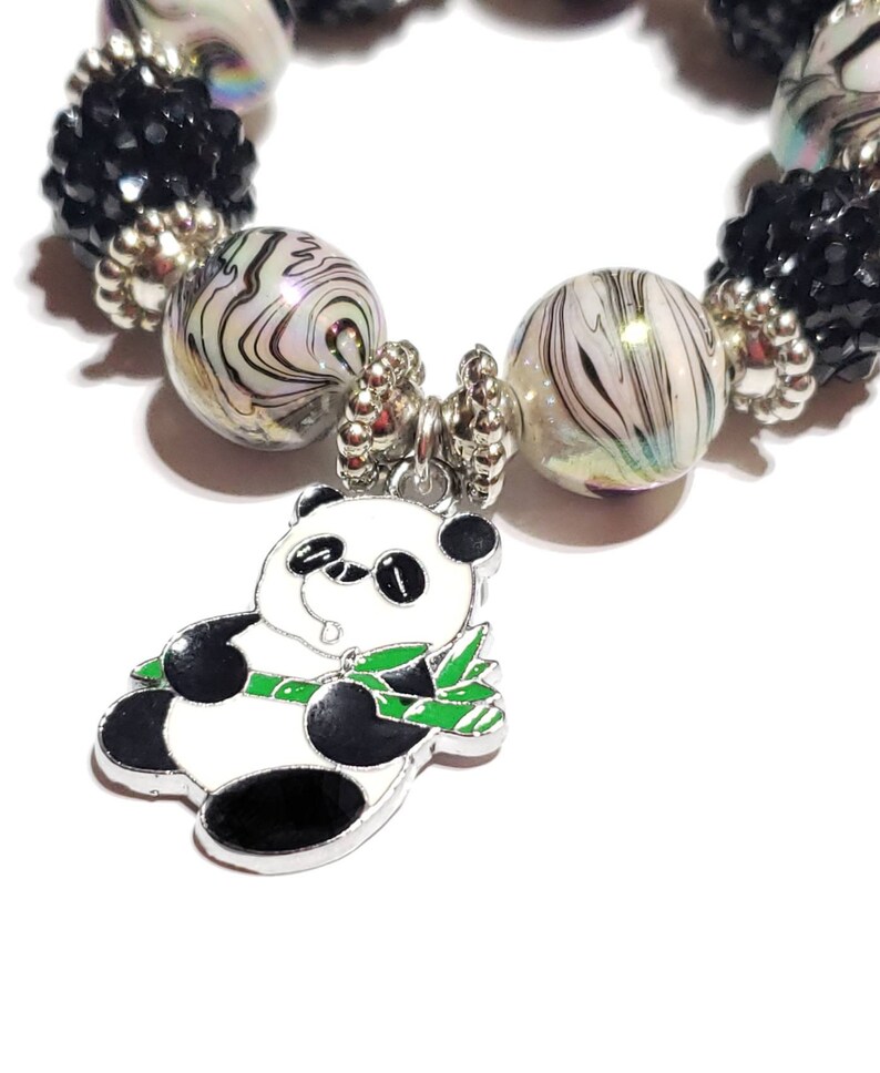 May include: A silver charm bracelet with black and white swirl beads, black crystal beads, and a panda bear charm holding bamboo.