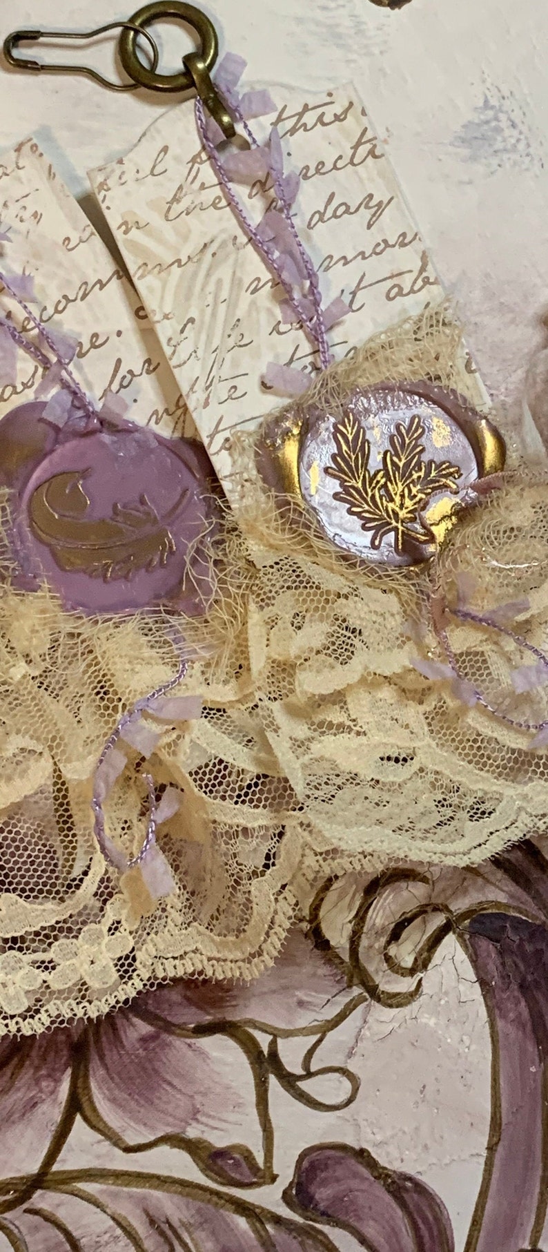 May include: Two vintage-style tags with purple wax seals and gold accents. The seals feature a feather and a sprig of leaves. The tags are tied together with a delicate lace ribbon and a gold safety pin.