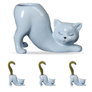 May include: A light blue ceramic cat-shaped planter with a curved body and a round opening. The cat is in a stretching pose with its eyes closed. Three smaller cat figurines with gold-colored tails are also shown.