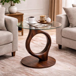 May include: A modern, round side table with a clear glass top and a unique, dark brown wooden base. The base features a distinctive open-circle design. The table is approximately 24 inches in diameter and 20 inches tall.