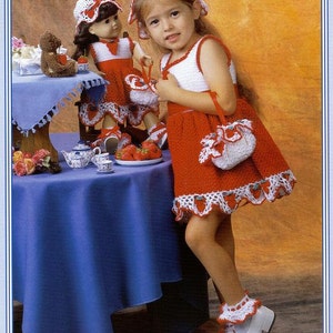 May include: Two girls wearing red and white crocheted dresses with strawberry accents. The girl on the left is a doll. The girls are sitting at a table with a blue tablecloth and teacups. The image is titled "Strawberries & Cream".