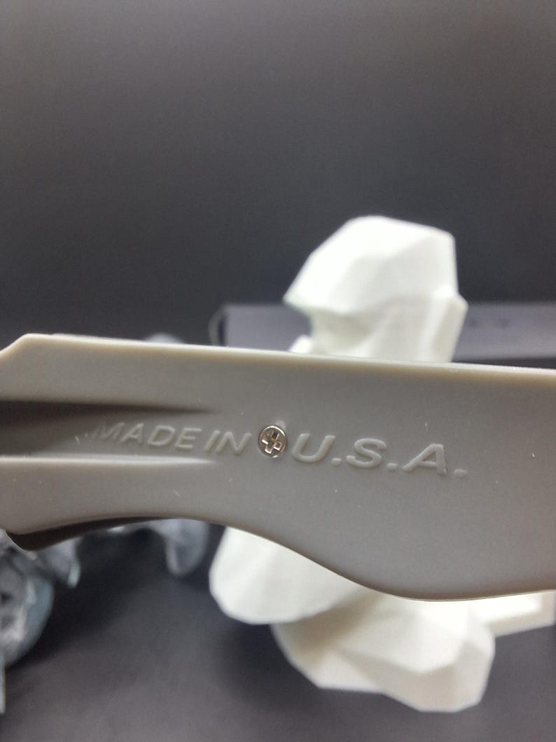 May include: Close-up of a gray plastic tool with the text "MADE IN U.S.A." printed on it. The tool has a small emblem next to the text. A white, geometric shape is in the background.