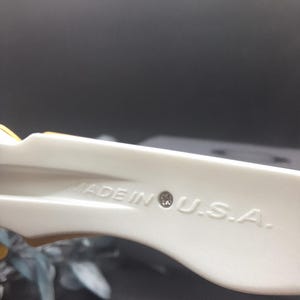 May include: Close-up of a cream-colored plastic object with the text "MADE IN U.S.A." stamped on its surface. The object has a curved shape and appears to be part of a larger item.