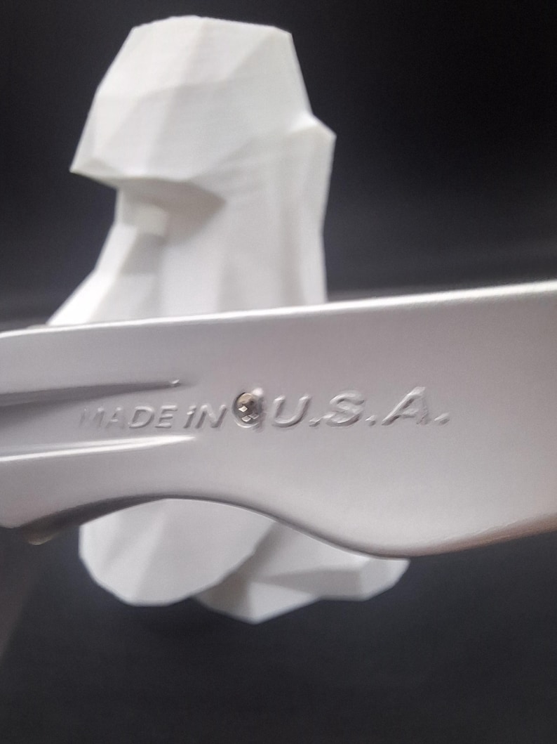 Puede incluir: Primer plano de una llave inglesa plateada con el texto "MADE IN U.S.A." grabado en el lateral. Una escultura geom&eacute;trica blanca en el fondo, sobre un fondo oscuro.