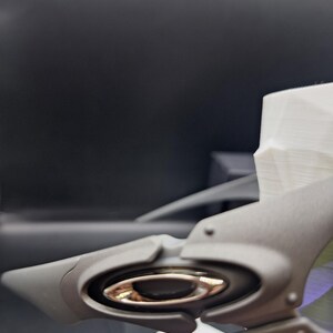 Op de afbeelding: Close-up van een grijs Oakley zonnebrilmontuur met een metallic gouden lensdetail. Het montuur heeft een strak, modern design met een prominent logo. De achtergrond is donker en onscherp.