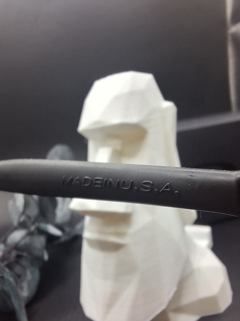 May include: A black object with the text "MADE IN U.S.A." is in front of a white, geometric sculpture of a head. The sculpture has a flat top and a defined nose and mouth. The background is dark.
