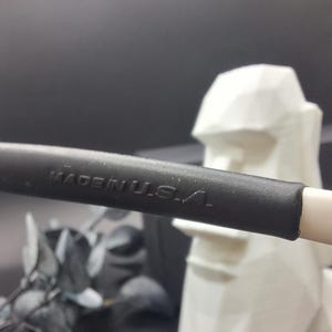 May include: Close-up of a black object with the text "MADE IN U.S.A." in white. The object is on a white surface, with a white geometric sculpture in the background. The background is dark.