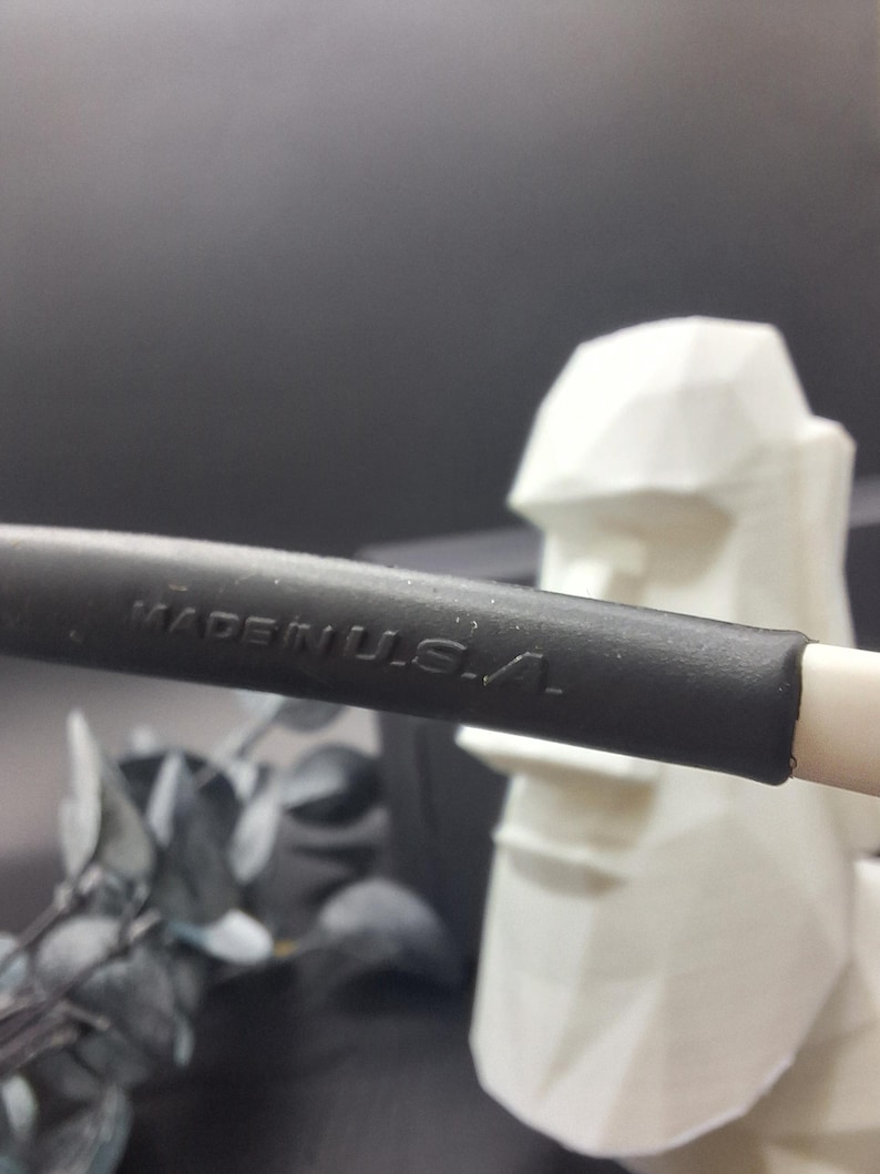 May include: Close-up of a black object with the text "MADE IN U.S.A." in white. The object is on a white surface, with a white geometric sculpture in the background. The background is dark.